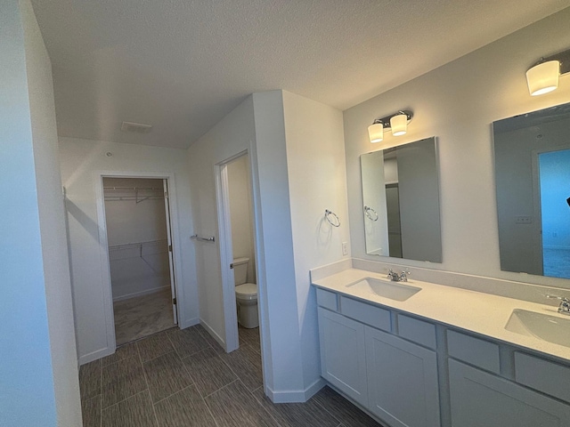 full bath featuring toilet, double vanity, a spacious closet, and a sink