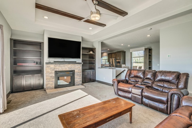 carpeted living room with built in shelves, ceiling fan, and a stone fireplace