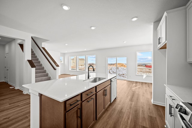 kitchen with a center island with sink, white cabinets, a sink, and stainless steel dishwasher