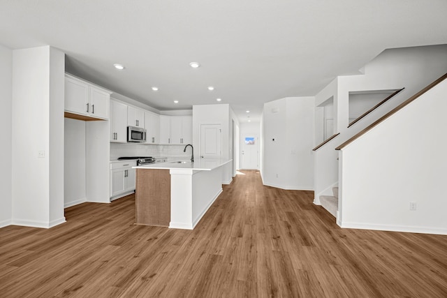 kitchen with a kitchen island with sink, a sink, white cabinetry, light countertops, and appliances with stainless steel finishes