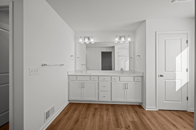 full bath featuring double vanity, wood finished floors, a sink, and visible vents