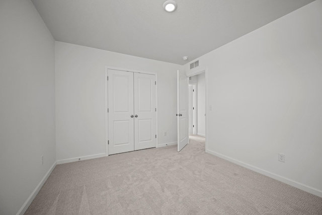 unfurnished bedroom featuring visible vents, baseboards, a closet, and light colored carpet