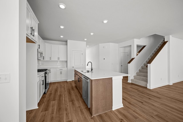 kitchen featuring stainless steel appliances, tasteful backsplash, open floor plan, a sink, and wood finished floors