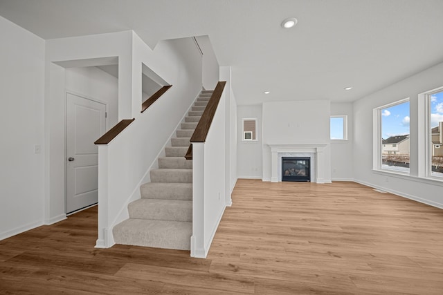 unfurnished living room featuring baseboards, a high end fireplace, light wood-style flooring, stairway, and recessed lighting