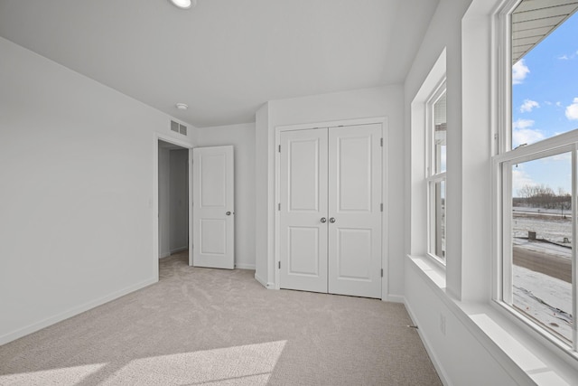 unfurnished bedroom featuring baseboards, visible vents, a closet, and light colored carpet