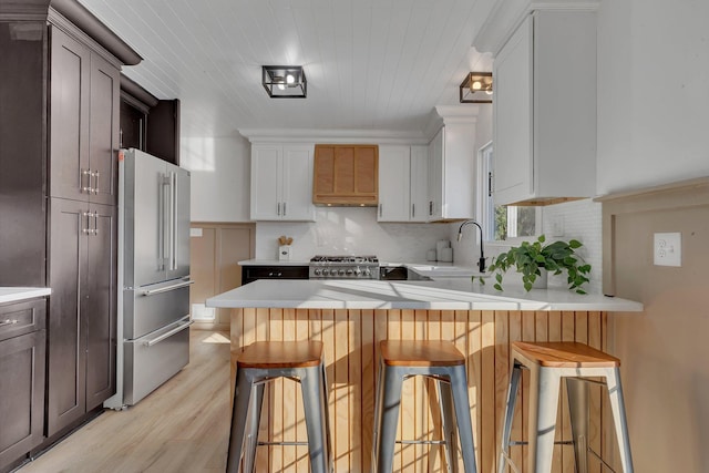 kitchen with a breakfast bar, high end fridge, backsplash, white cabinetry, and stove