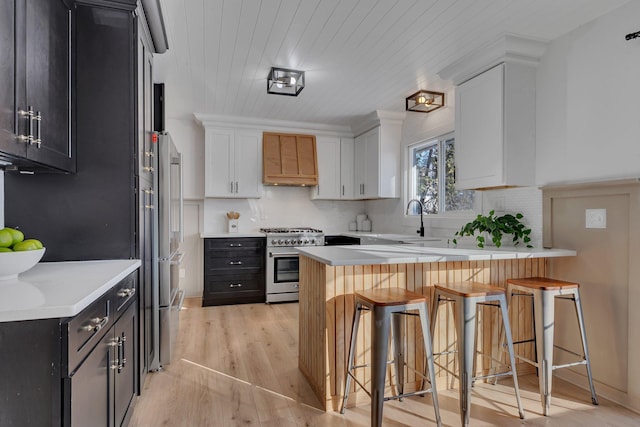 kitchen featuring light hardwood / wood-style flooring, high end stainless steel range oven, white cabinets, a kitchen bar, and custom exhaust hood