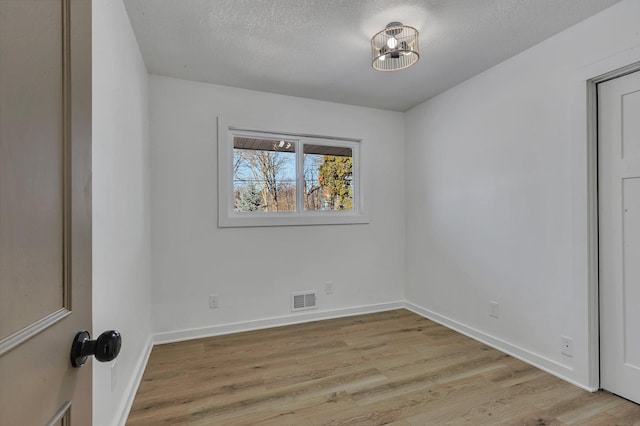 unfurnished room with light hardwood / wood-style flooring and a textured ceiling