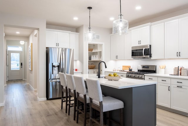 kitchen featuring an island with sink, a kitchen breakfast bar, stainless steel appliances, light wood-type flooring, and a sink