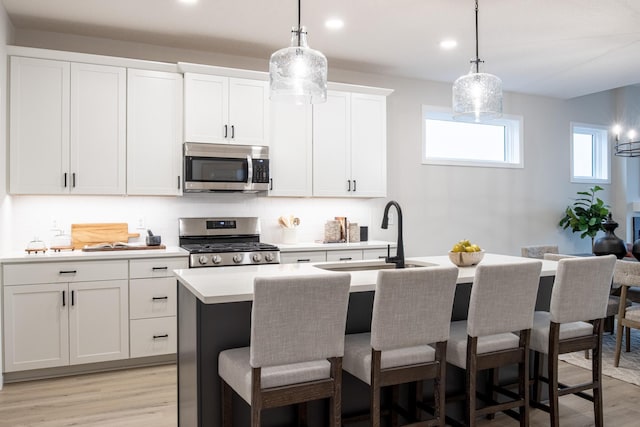 kitchen featuring light wood finished floors, a kitchen island with sink, stainless steel appliances, light countertops, and a sink