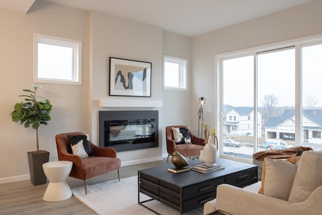 living area with a glass covered fireplace, wood finished floors, and baseboards