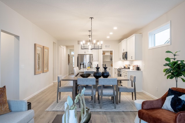 dining area featuring light wood-type flooring, baseboards, and a notable chandelier