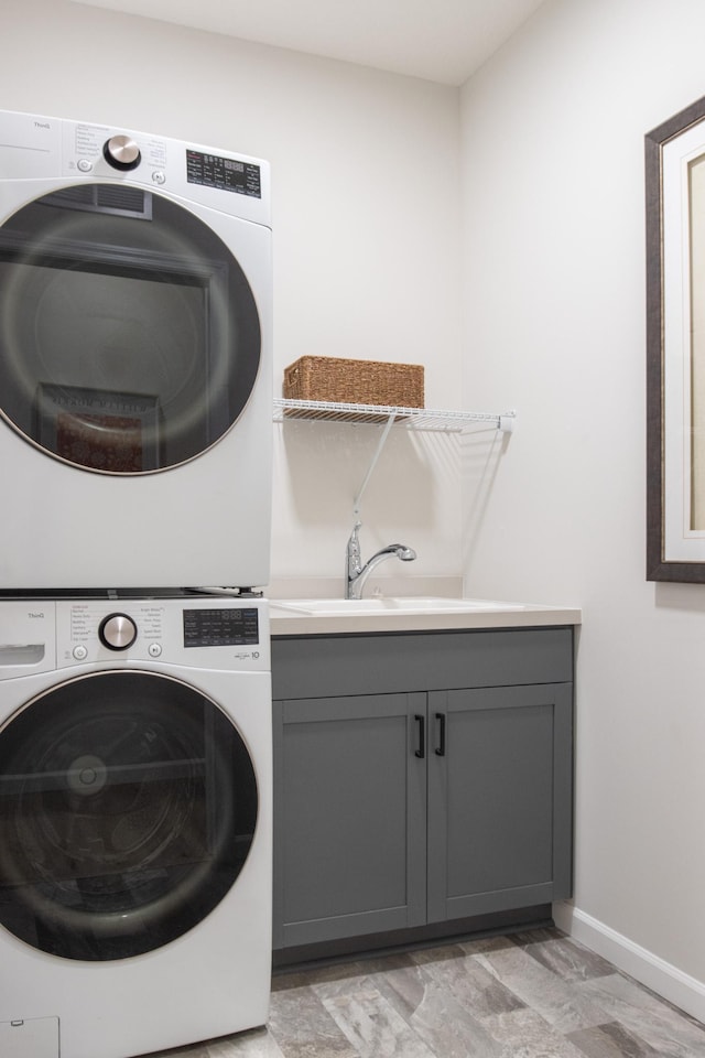 washroom with stacked washer / dryer, a sink, cabinet space, and baseboards