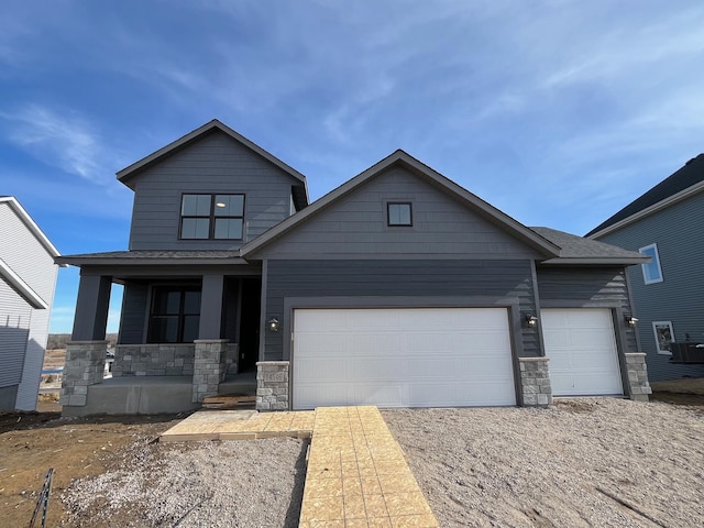 view of front of house featuring a garage, covered porch, stone siding, and central AC unit