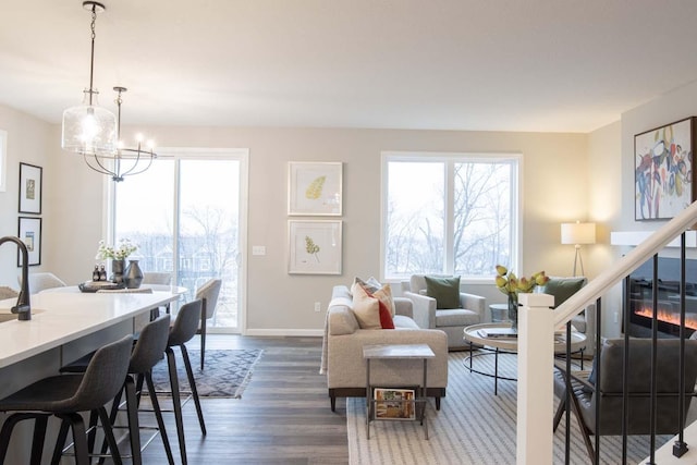 living room featuring baseboards, dark wood finished floors, a notable chandelier, and a glass covered fireplace