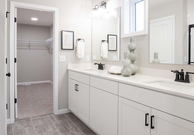 bathroom with a walk in closet, a sink, baseboards, and double vanity