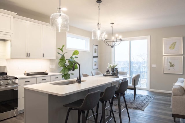 kitchen featuring a center island with sink, light countertops, stainless steel range with gas stovetop, a sink, and a kitchen breakfast bar