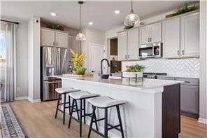 kitchen featuring a kitchen island with sink, hanging light fixtures, backsplash, and stainless steel appliances