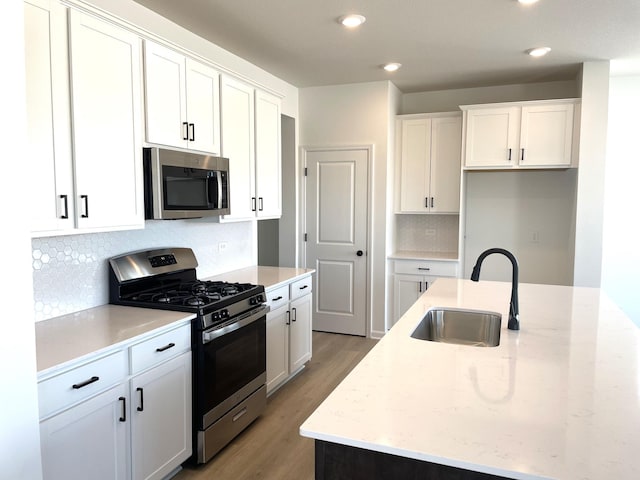 kitchen featuring stainless steel appliances, white cabinets, a sink, and an island with sink