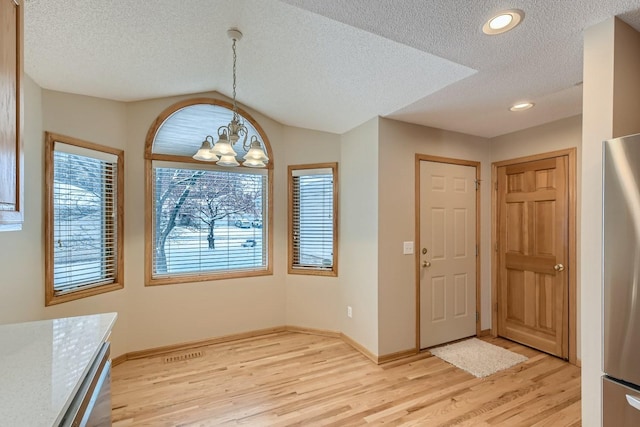 entryway with lofted ceiling, a notable chandelier, light hardwood / wood-style floors, and a textured ceiling