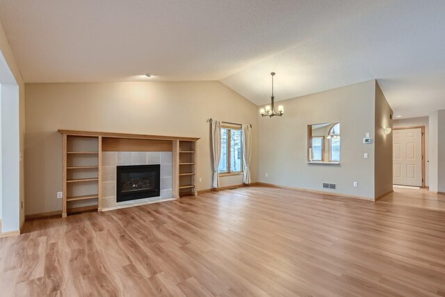unfurnished living room with visible vents, lofted ceiling, a fireplace, a chandelier, and light wood finished floors