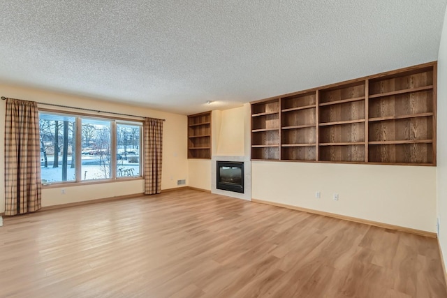 unfurnished living room with baseboards, a textured ceiling, a glass covered fireplace, and light wood finished floors