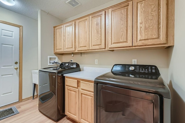 clothes washing area featuring independent washer and dryer, cabinet space, a textured ceiling, light wood-type flooring, and visible vents
