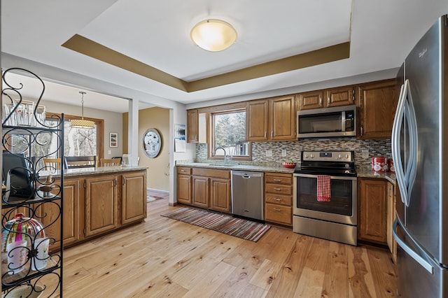 kitchen featuring hanging light fixtures, light stone countertops, appliances with stainless steel finishes, and a tray ceiling