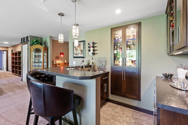 kitchen with light carpet, dark countertops, a breakfast bar area, decorative light fixtures, and a sink