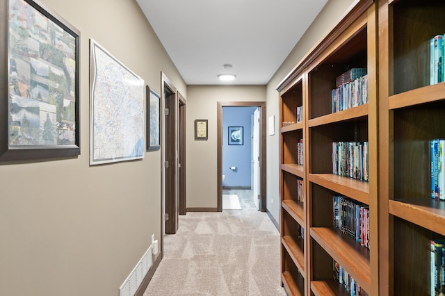 corridor with baseboards, visible vents, and light colored carpet