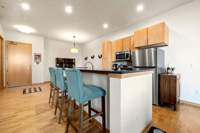 kitchen featuring recessed lighting, a kitchen breakfast bar, light wood-style floors, appliances with stainless steel finishes, and decorative light fixtures