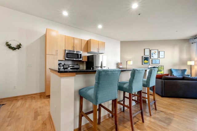 kitchen with a kitchen bar, light wood-style flooring, backsplash, open floor plan, and appliances with stainless steel finishes