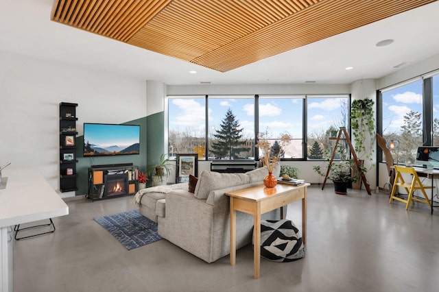 living area featuring finished concrete flooring, a healthy amount of sunlight, recessed lighting, and a glass covered fireplace