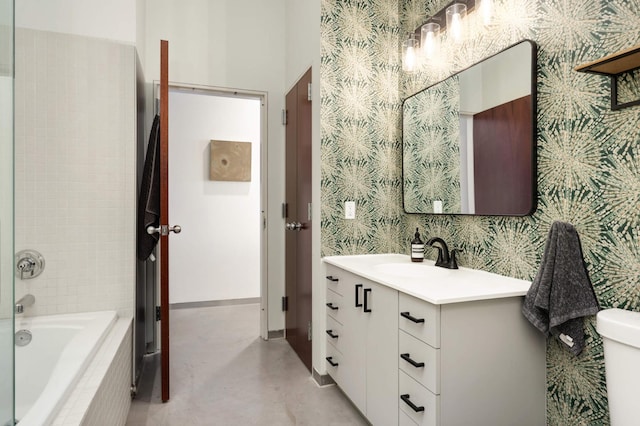 full bathroom with a relaxing tiled tub, toilet, vanity, baseboards, and wallpapered walls