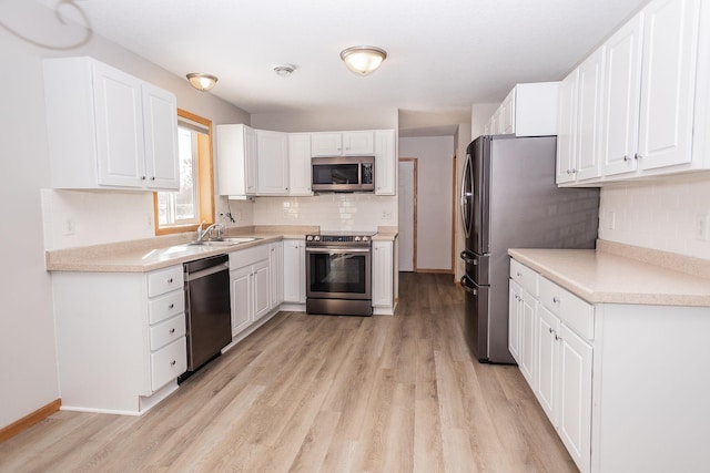 kitchen with appliances with stainless steel finishes, sink, white cabinets, decorative backsplash, and light hardwood / wood-style floors