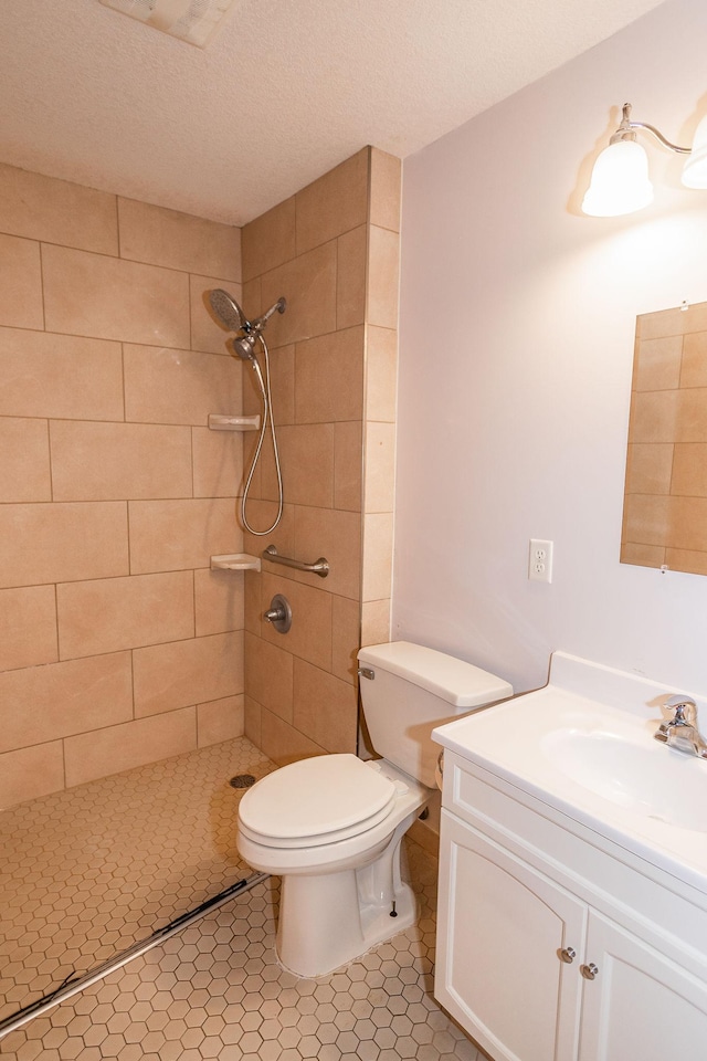 bathroom featuring tiled shower, vanity, toilet, and a textured ceiling