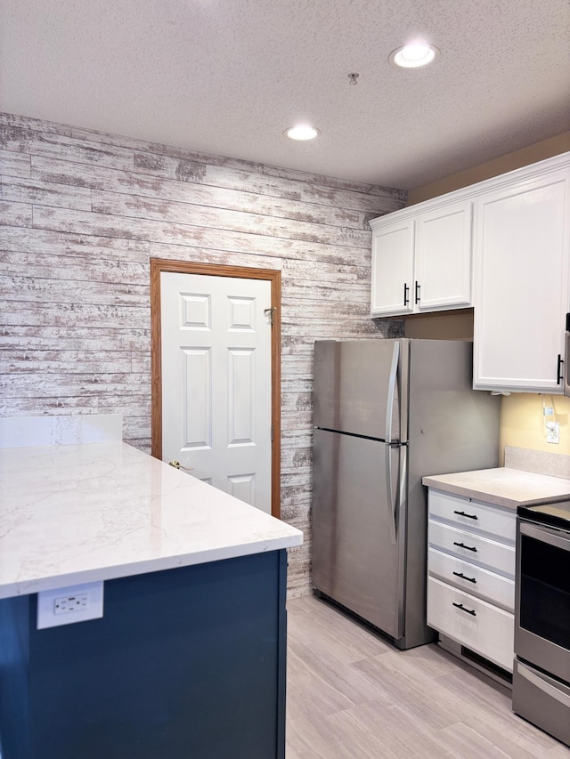 kitchen with white cabinets, light stone counters, stainless steel appliances, a textured ceiling, and light hardwood / wood-style flooring