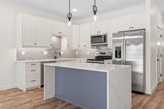 kitchen featuring a kitchen island, pendant lighting, stainless steel appliances, light hardwood / wood-style floors, and white cabinets