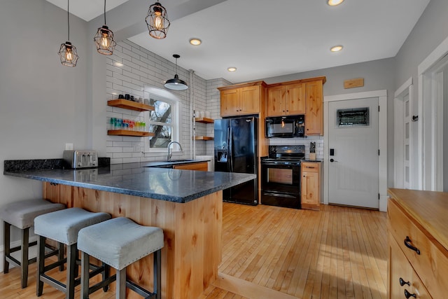 kitchen featuring a kitchen breakfast bar, kitchen peninsula, pendant lighting, decorative backsplash, and black appliances