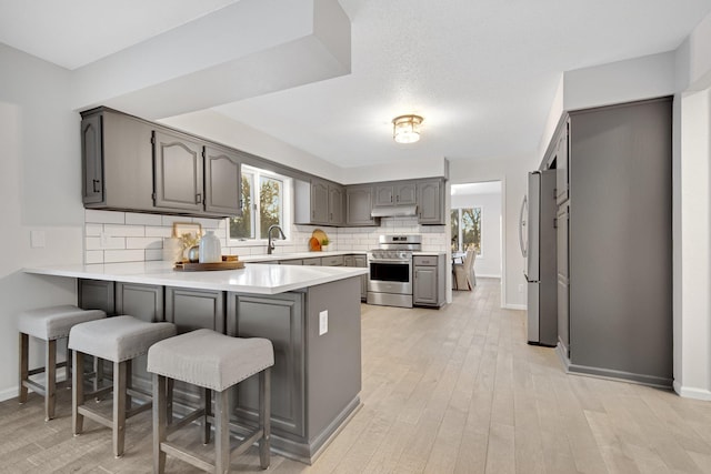 kitchen with gray cabinetry, a kitchen breakfast bar, kitchen peninsula, and appliances with stainless steel finishes