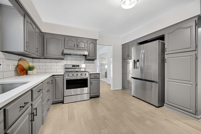 kitchen featuring gray cabinets, appliances with stainless steel finishes, backsplash, and light wood-type flooring