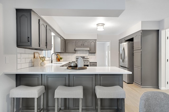 kitchen featuring appliances with stainless steel finishes, gray cabinetry, a kitchen breakfast bar, and kitchen peninsula