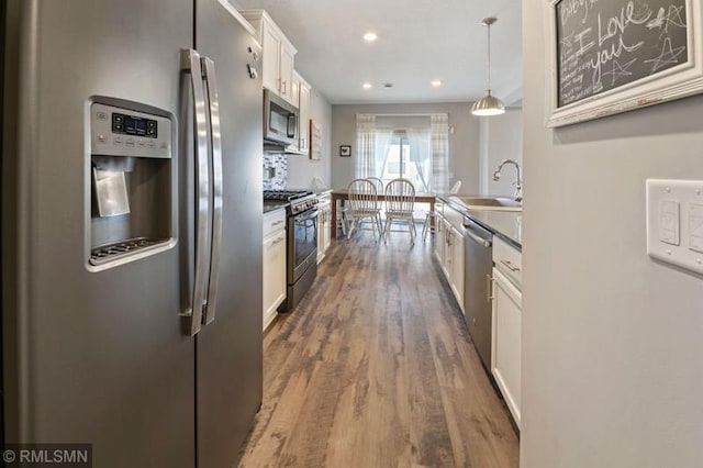 kitchen featuring sink, appliances with stainless steel finishes, white cabinetry, hanging light fixtures, and dark hardwood / wood-style flooring