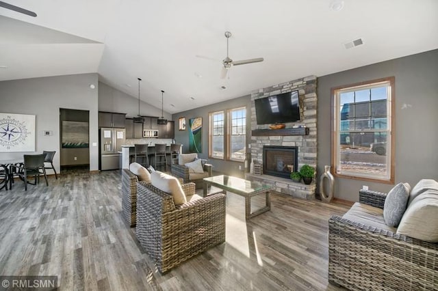 living room with hardwood / wood-style flooring, ceiling fan, a stone fireplace, and vaulted ceiling