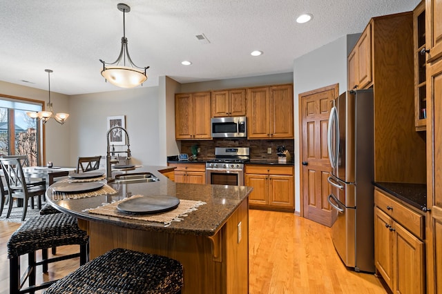 kitchen featuring stainless steel appliances, brown cabinetry, a kitchen bar, and a center island with sink