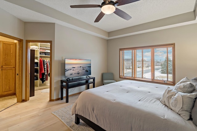 bedroom with a closet, a spacious closet, ceiling fan, a textured ceiling, and light wood-type flooring