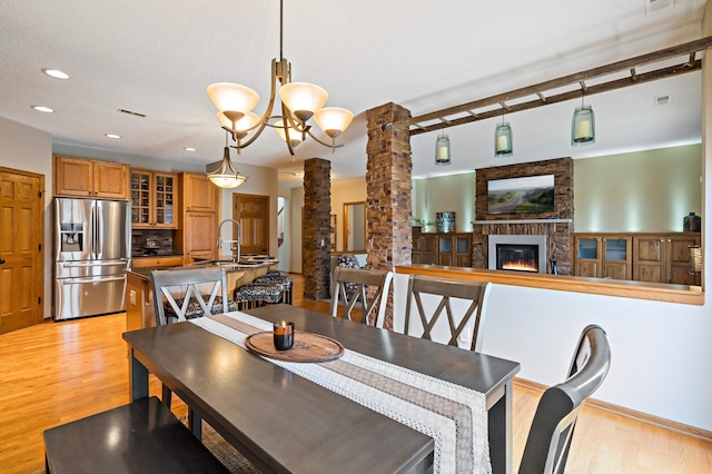 dining room featuring recessed lighting, visible vents, light wood-style floors, a brick fireplace, and ornate columns