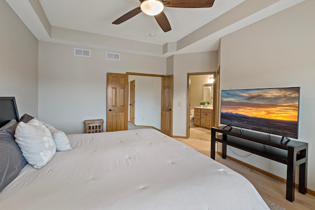 bedroom featuring light wood-style floors, a raised ceiling, visible vents, and baseboards