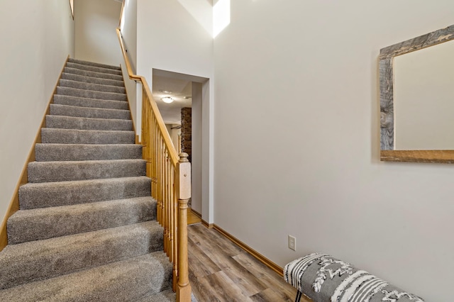 stairs with a towering ceiling, baseboards, and wood finished floors