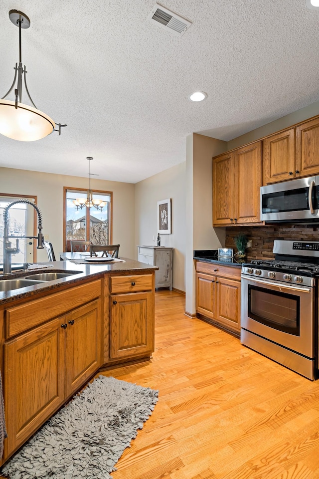 kitchen with stainless steel appliances, hanging light fixtures, dark countertops, and a sink